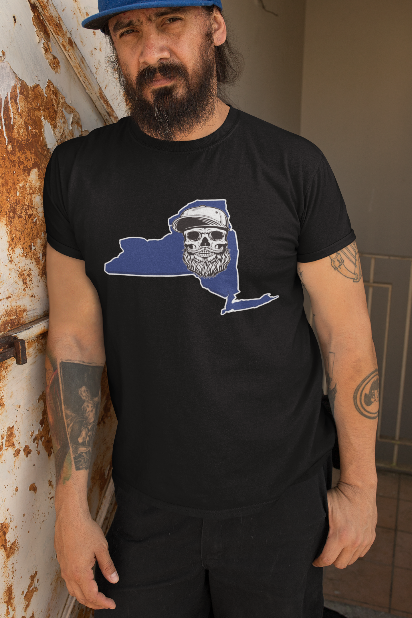 Man wearing a black t-shirt with a graphic design of a state map and skull, leaning against a wall.